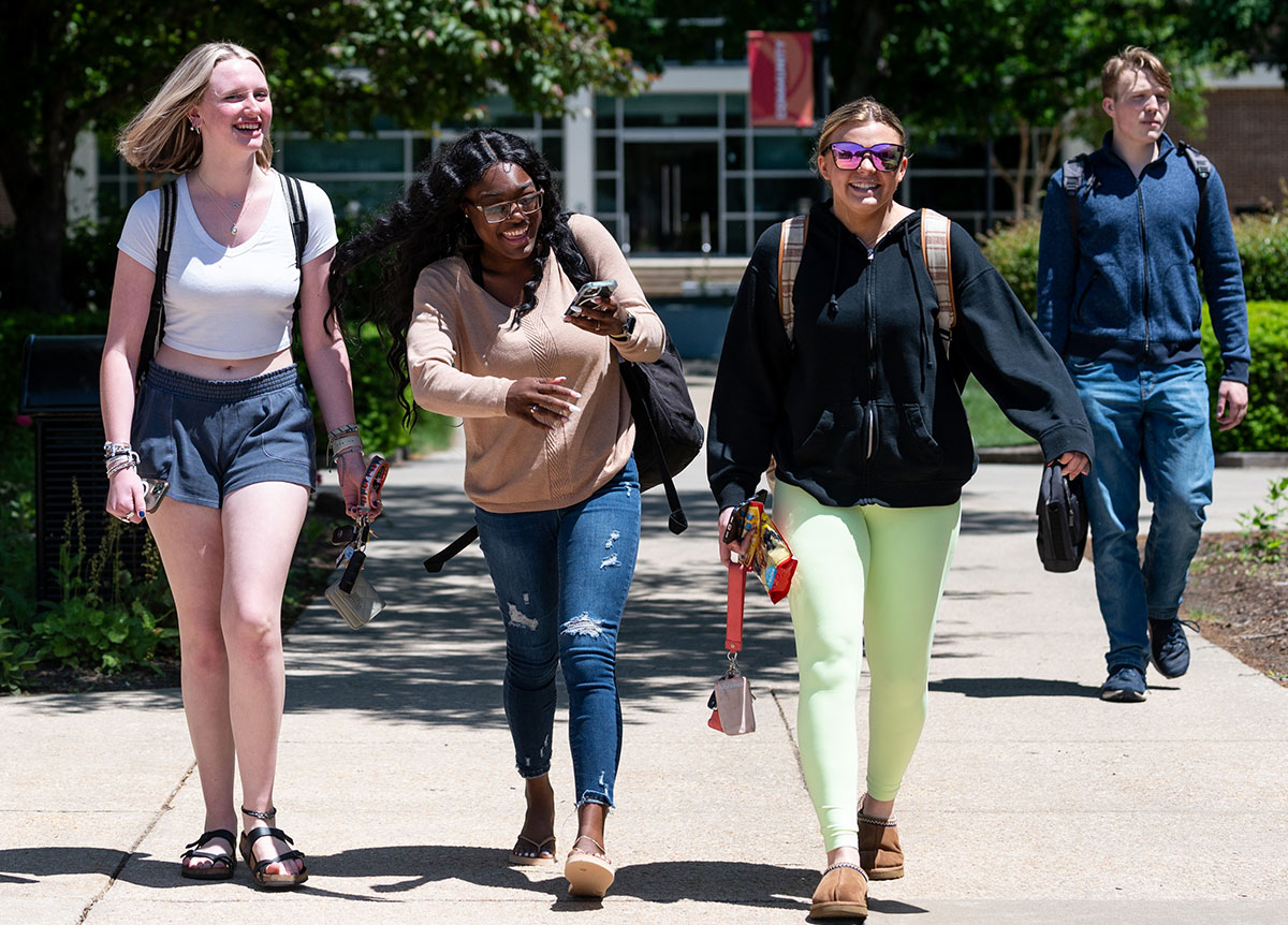Four students walking across campus, smiling and talking.